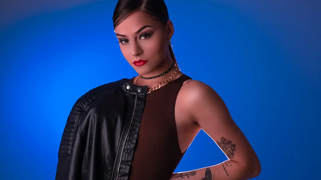 Fashion portrait of a woman with a black leather jacket over her shoulder against a blue background